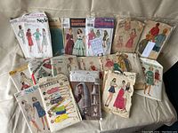 Photo showing multiple vintage sewing pattern envelopes from brands like Simplicity, Butterick, McCall's, and Style featuring women's clothing styles from mid-20th century.