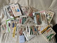 Photo displaying a collection of vintage sewing patterns from various brands including Simplicity, Style, Vogue, McCall's, and Butterick with illustrated covers showing women's and children's clothing designs.