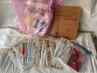 Lot of vintage sewing pattern envelopes along with an old typewriting textbook on white background.