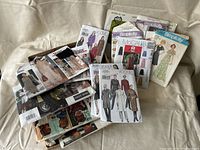 Photo showing a collection of vintage sewing pattern envelopes laid out on a fabric surface, including Vogue, Simplicity, and McCall's patterns.