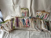 Photo showing assortment of 21 vintage sewing pattern envelopes with images of clothing styles for women.