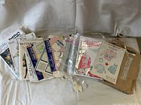 Lot of vintage sewing transfer patterns in original envelopes arranged on fabric background.