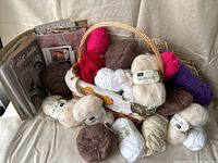 Lot shows a collection of yarn skeins in different colors and types arranged with a basket and knitting patterns.