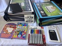 Photo showing a stack of blue and black 3-ring binders, a small black leather phone wallet, an eight-pack of assorted Sharpie markers, a word hunt activity pack with scented crayons, and a fridge magnet with a humorous text message.