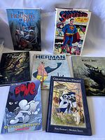 Photo showing all seven graphic novels and comics together on a white backdrop, visible titles and cover artwork clear.