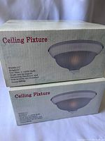 Two boxes of brand new ceiling light fixtures, sealed. Boxes show product image and specifications including size 11" width x 6" height, max 60W bulb, white finish.
