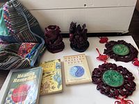Wide view showing the two red dragon figurines, three wellness books, and the large drawstring bag placed next to them on a wooden floor against a white background.