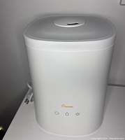 Photo of white Crane humidifier and diffuser showing front panel with three touch buttons and brand name.