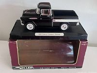 Side view of black 1957 Chevrolet Cameo pickup truck model mounted on black display base with label.