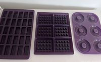 Three purple silicone molds on white surface: mini bar mold (16 cavities), waffle mold (4 sections), donut/bagel mold (4 round cavities).