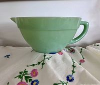 Side profile showing the opaque green jadeite color, spout and handle, placed on floral cloth.