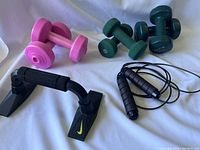 Photo showing all items including pairs of dumbbells, Nike push-up grips, and skipping rope spread on white surface.