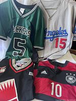 Four sports jerseys, front view showing details including numbers, colors and logos