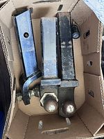 Overhead photo of the three hitch ball mounts arranged side by side in a cardboard box showing rust, wear, and overall used condition.