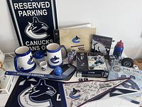 Photo of various Canucks merchandise including mugs, hockey accessories, signed pennant flag, puzzles, and parking sign.