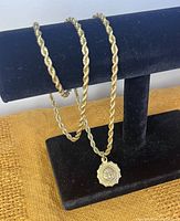 Gold-tone chain necklace on black jewelry display stand showing thick rope chain and sun pendant with facial details