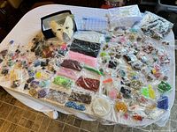 Overall view showing a large number of bead bags spread over a table, including both colorful beads and beading tools/storage boxes.
