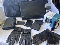 Full lot displayed showing all items: black Buxton laptop case, nylon laptop tote bag, multiple black leather wallets and card holders, two pairs of black gloves (one leather), Northern Lights mug in box, and black flashlight.
