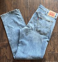 Front and rear view of light blue Levi's 541 Athletic Taper Fit jeans laid flat on wooden floor. Shows back pocket, leather Levi's logo patch, and front pockets with button fly.