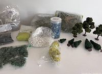 Overview of miniature crafting materials including bags of decorative sand, rocks, moss and seven model trees