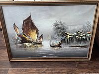 Full view of the framed oil painting showing boats and waterfront village