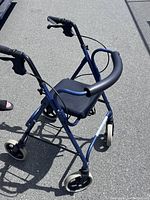 Overview of blue four-wheeled rolling walker with padded seat and backrest, and hand brakes on handles.