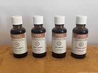 Four amber glass bottles of Aveda Key Element essential oils labeled 10 Earth Nature, 17 Water Nature, 22 Air Nature, 26 Infinity Nature on a brown surface.
