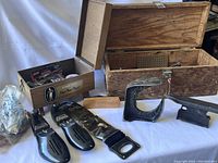 Shows two wooden boxes with assorted shoe shine and repair equipment outside the boxes on white surface, including two shoe stretchers and brushes.