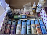 Photo showing multiple bottles of Plaid Gallery Glass liquid leading, window colors, metallic paint, glitter powder, brushes and other painting tools inside the box.