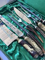 Top view of set showing 6 tools with engraved blades, antler handles, in green-lined box