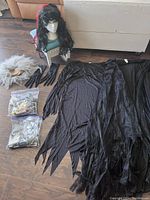 Full view of witch costume components laid out including black dress, cloak, gloves, two bags of makeup/accessories, and wigs on a chair.