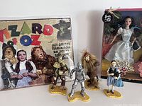 Metal Wizard of Oz sign with classic movie characters Judy Garland as Dorothy and others in color; partially shown Dorothy Barbie in box and ornaments in front.