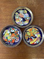 Three vintage Rosenthal wall plates with intricate colorful Aladin-themed artwork, blue background and gold borders laid out on wooden surface.