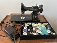 Singer machine placed on wood table with front-facing accessories tray and foot pedal.