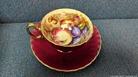 Photo showing the set from the side angle highlighting the fruit design inside the cup and the burgundy saucer with gold trim