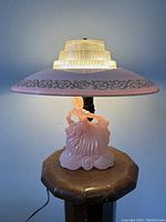Front view of the lamp lit, showing entire lamp including the pink glass ornamental shade with silver scroll work and clear tiered top diffuser.