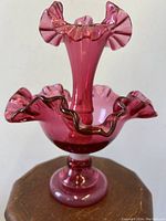 Front view of the cranberry glass epergne showing trumpet-shaped top with ruffled edges and darker trim detail, mounted on a pedestal base.