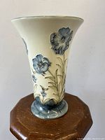Front view showing the tube-lined blue floral artwork on cream ceramic vase with flared top and rounded grayish-blue base.