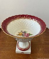 Front view showing interior floral decoration and burgundy scalloped rim with gold accents.