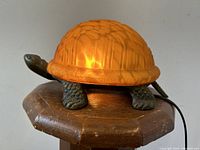 Lamp lit showing amber glass shell on metal tortoise base, three-quarter view
