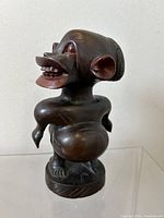 Front three-quarter view of the carved wood figure showing the facial features, arms, rounded belly, and base.