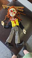 Full view of the vintage clown string puppet laid flat, showing wooden cross bar, yarn hair, painted face, and fabric clothing.