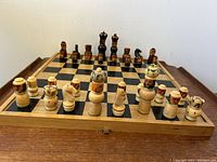 Chessboard set up with all chess pieces placed on the board in starting positions, showing both light and dark carved figural pieces with painted details.