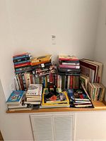 Collection of assorted books stacked against a white wall with visible titles on natural science, travel, and history.