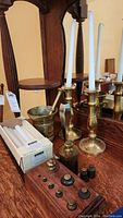 Two brass candlesticks with white taper candles, a partial box of white taper candles, and a brass mortar on a wooden surface.