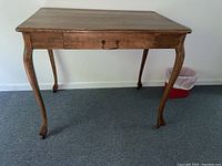 Full front view of a wooden desk showing the single drawer with metal handle and curved legs with castors.