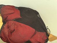 Black mesh bag containing red and black fabric cornhole bags.