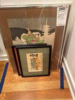 Four framed Japanese woodblock prints, the two largest approximately 18x14 inches, leaning against a wall on hardwood floor.