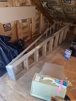 Full view of folding ladder extended out, placed on a wooden floor in an attic space with insulation visible on walls.