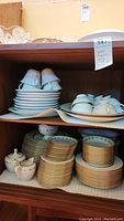Shelved Lenox china set showing stacked plates, bowls, and serving items with gold trim and floral patterns.